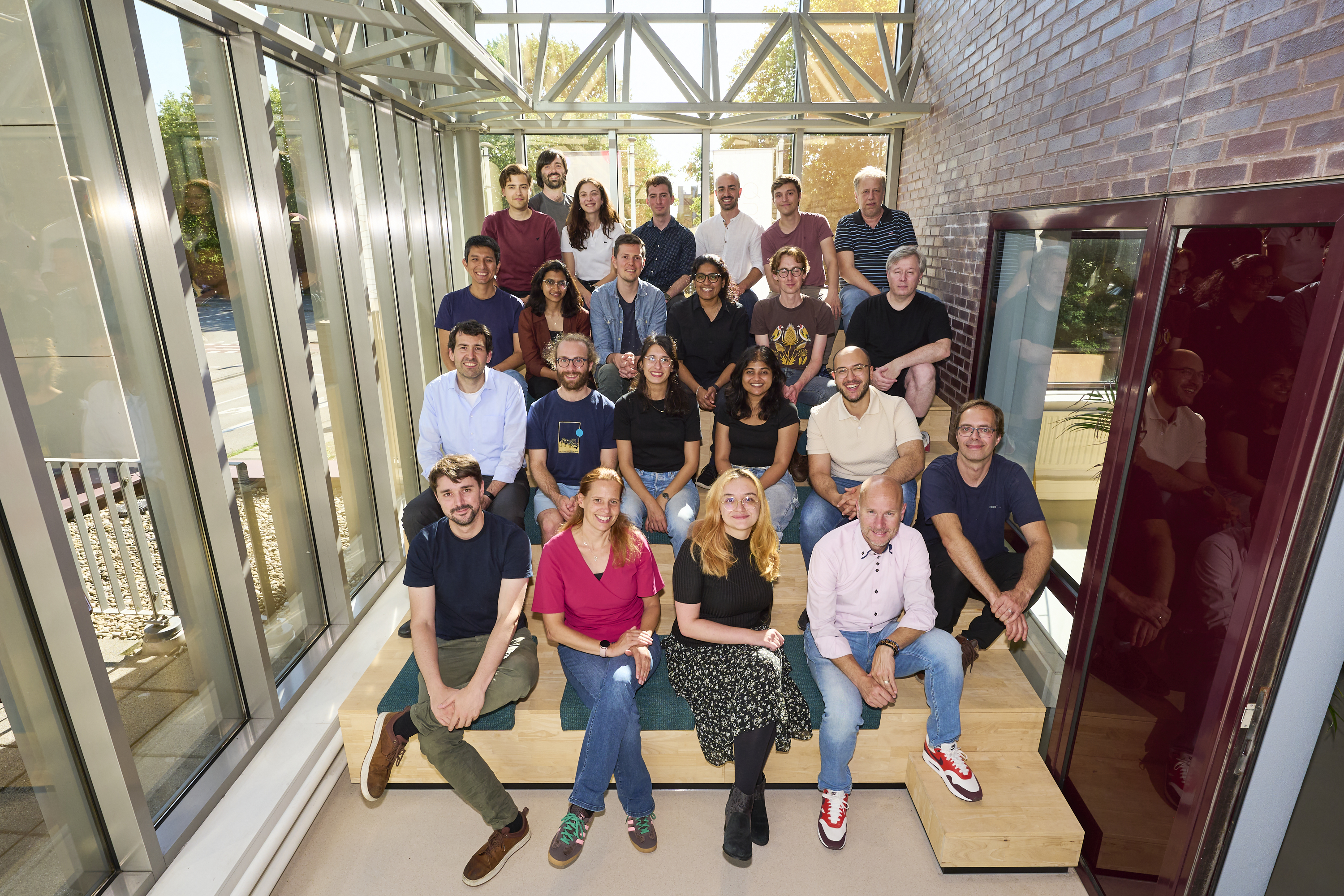 Twenty-three people from the Q*Bird team sit posed in their office space.